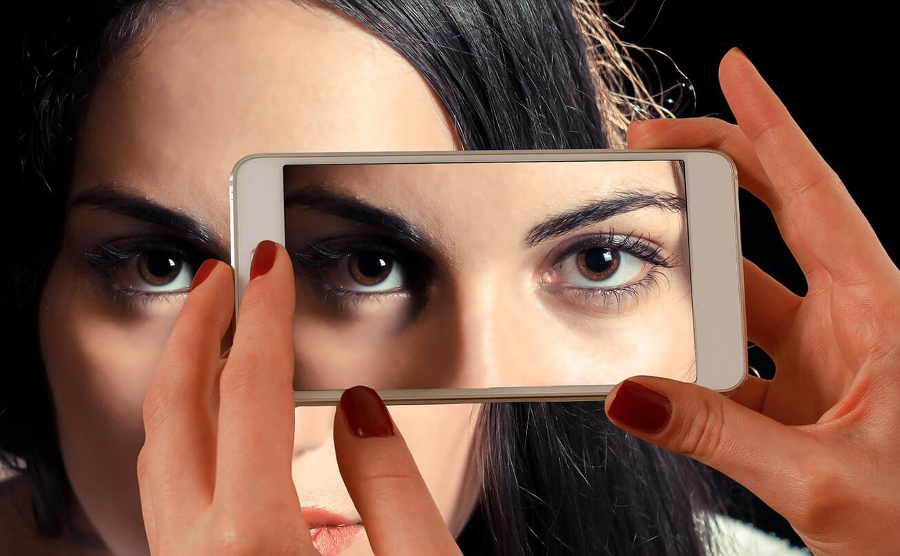 Woman looking at cell phone camera with her eyes reflected back